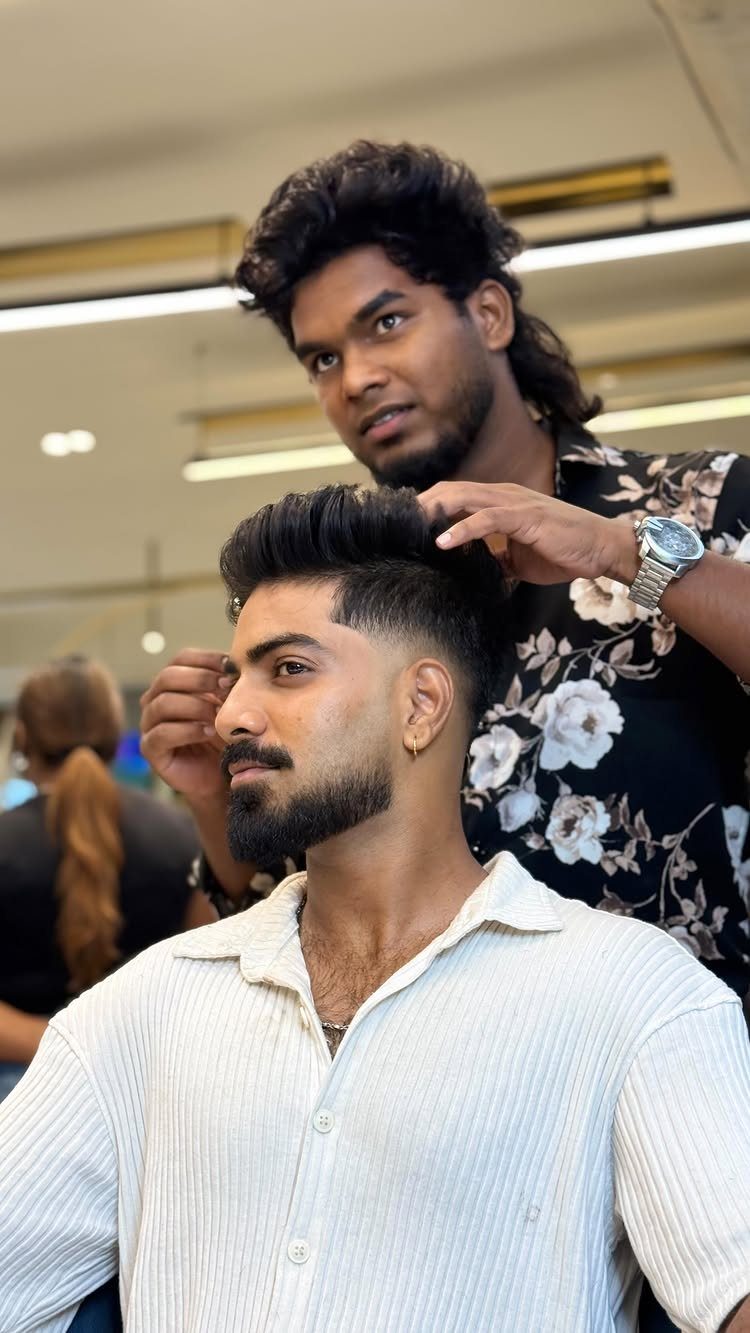 Man with a tousled mid fade haircut being styled by a barber in a shop.