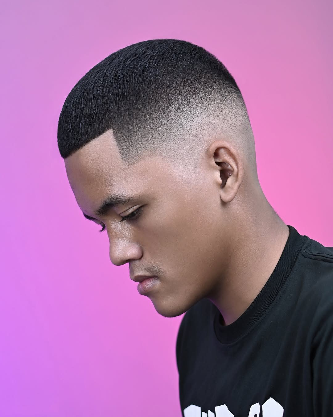 Man with a bald mid fade haircut and short top against purple background