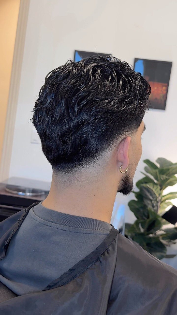 Man with dark wavy hair and a drop fade haircut seen from behind.