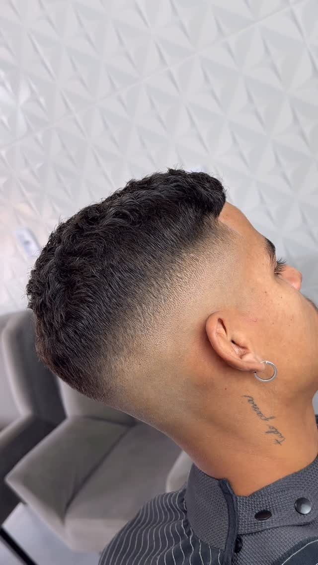 Man with a high fade haircut and curly top in a side profile view.