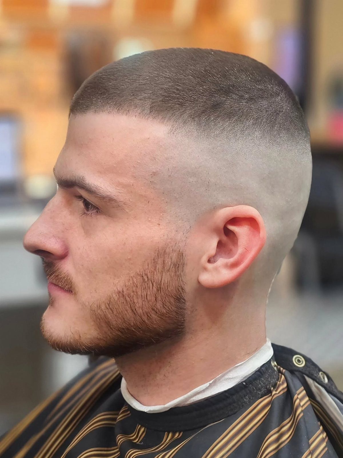 Man with a high skin fade haircut and short beard wearing a barber cape.