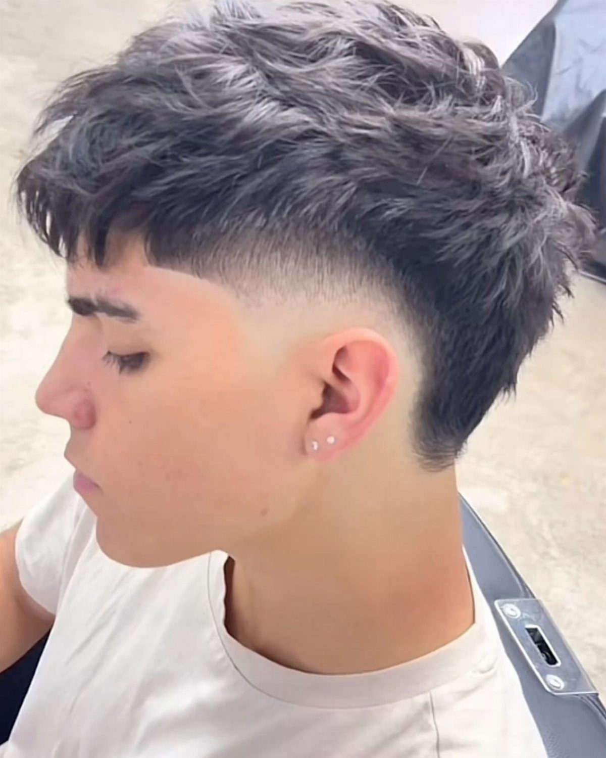Young man with a high skin fade and textured, messy wavy hair on top.