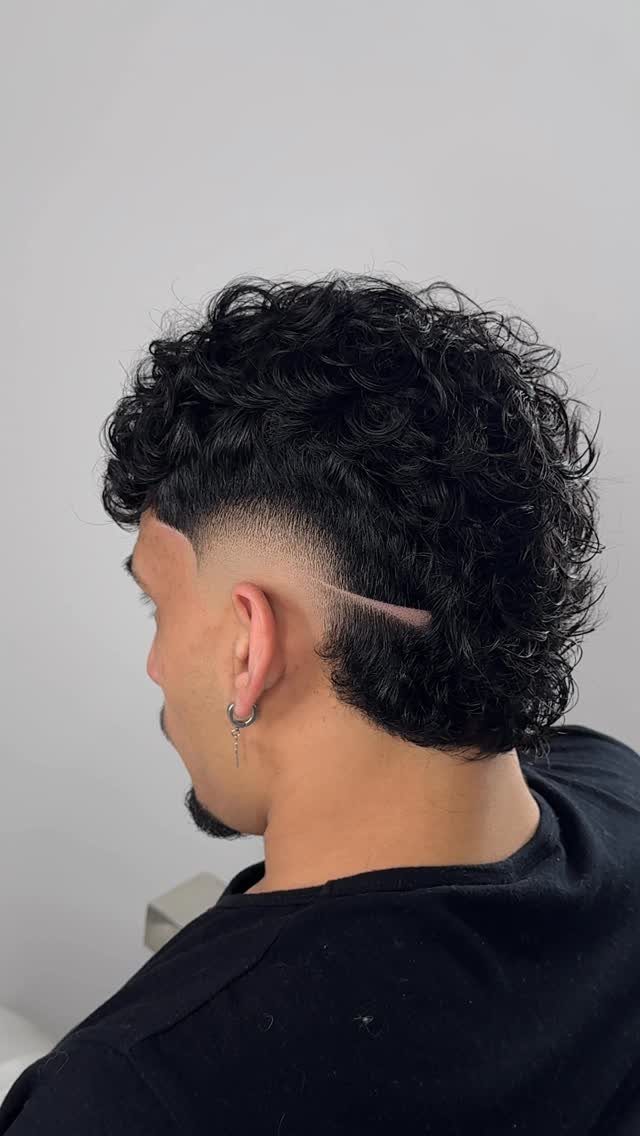 Man with a curly mid burst fade and a shaved line detail.