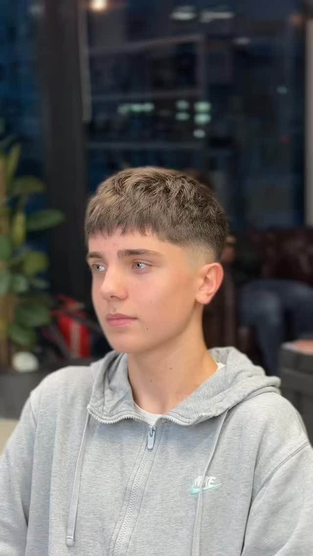 Young man with a mid fade haircut and short fringe wearing grey hoodie.