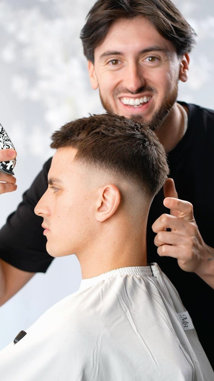Barber smiling behind a man with a fresh mid fade haircut and white cape.