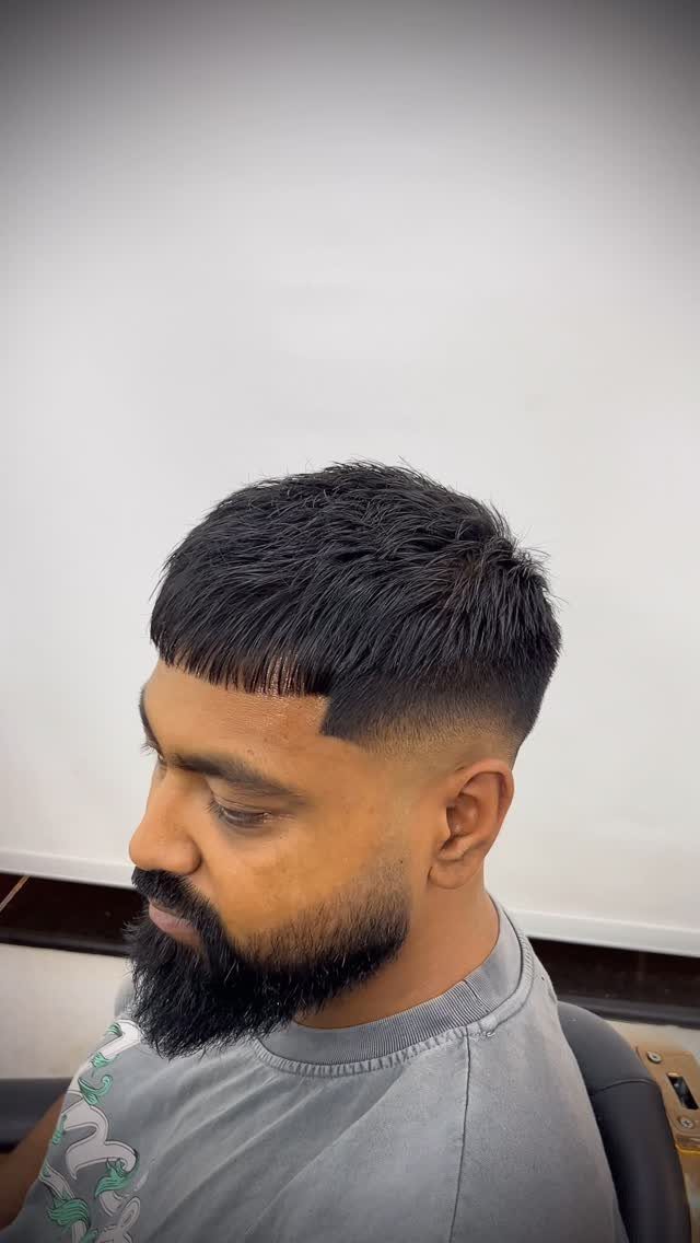 Man with a mid skin fade haircut and a full dark beard.