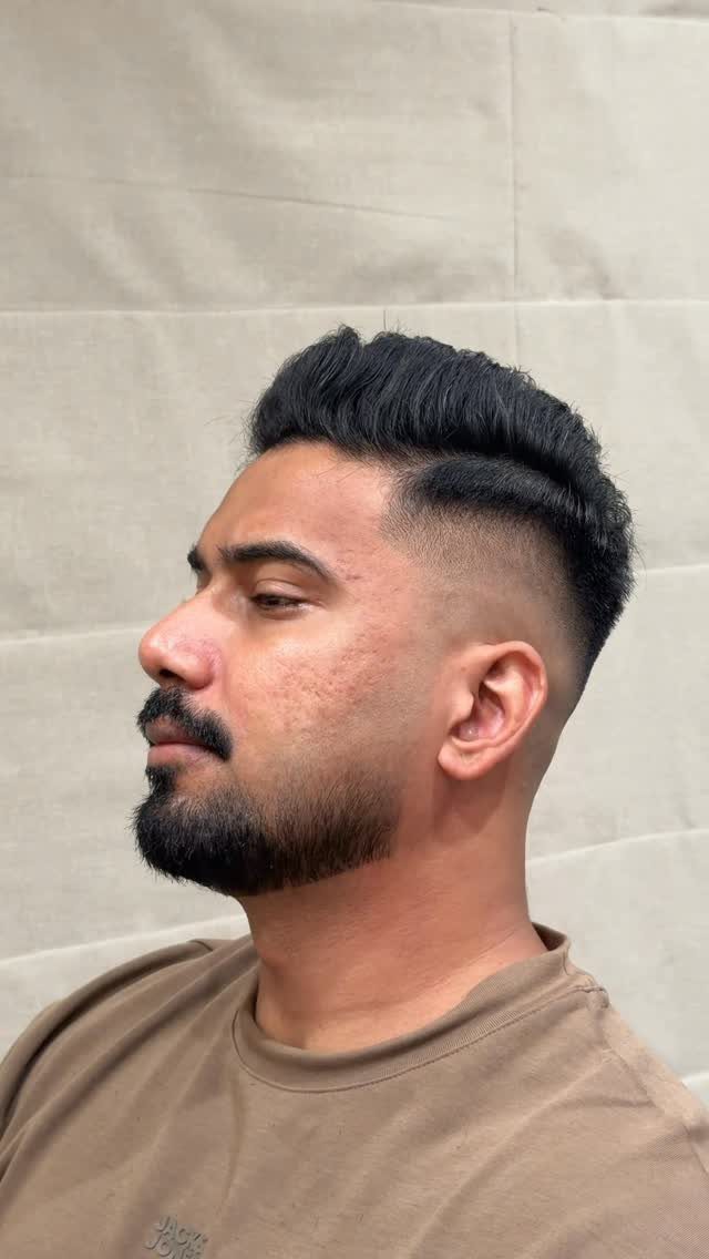 Man with a skin fade haircut and groomed beard against a beige background.