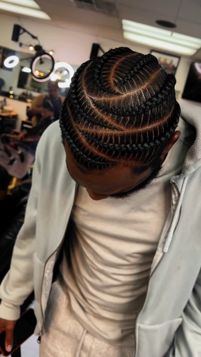 Man with dark hair styled in curved cornrow braids wearing a grey hoodie.