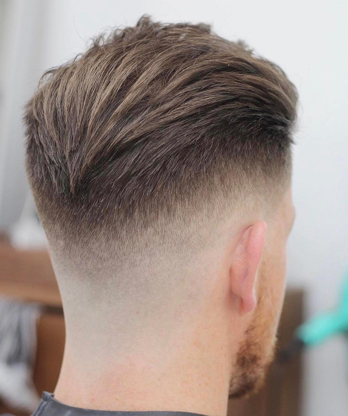 Man with brown hair brushed back and a high skin fade haircut.