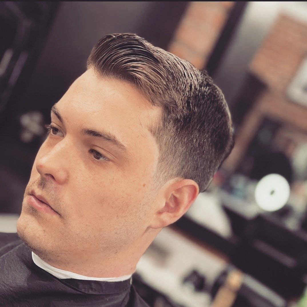 Man with a side-parted comb over haircut and tapered sides in a barbershop.