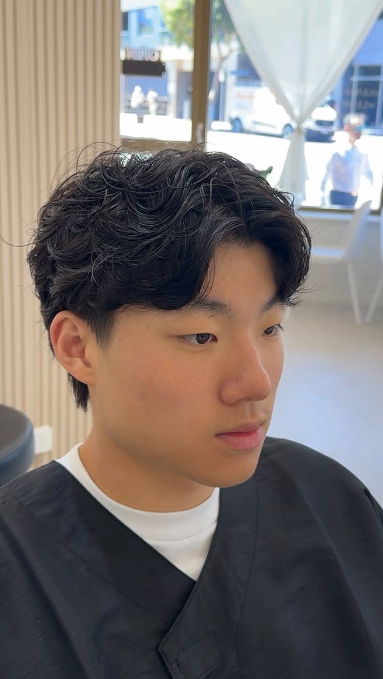 Young man with a Korean perm featuring soft, dark, medium-length wavy curls.