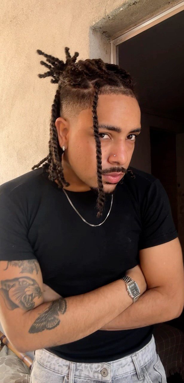 Man with medium length dreadlocks and shaved sides posing with arms crossed.