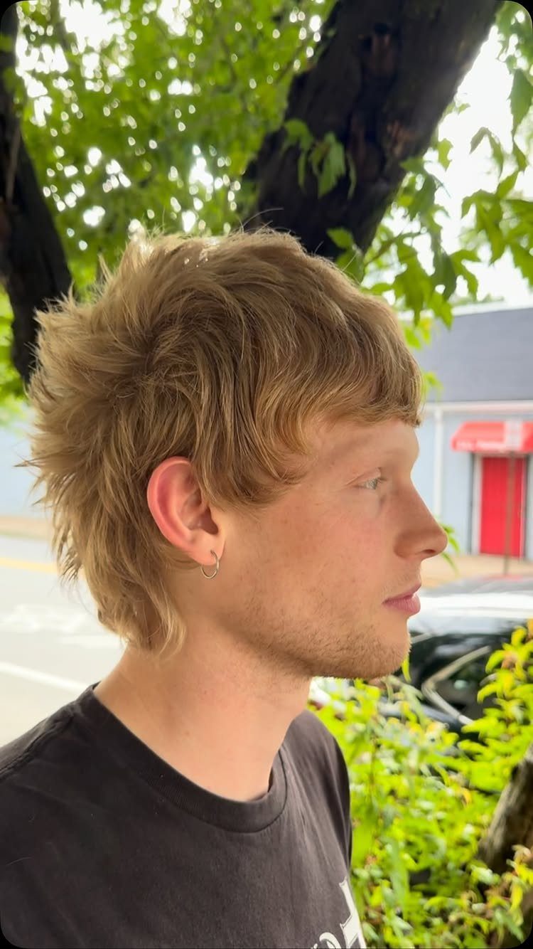 Young man with a choppy, layered medium blonde shag haircut in a side profile.