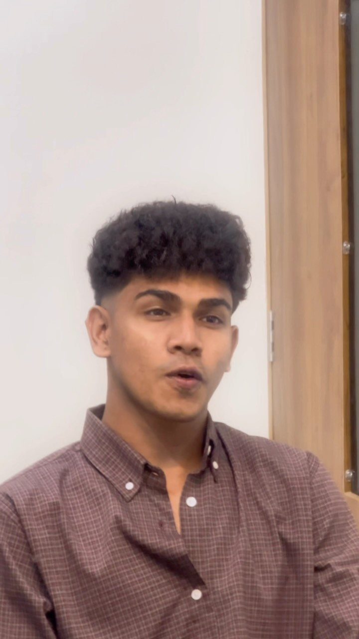 Young man with voluminous dark messy curls and short sides wearing brown shirt.