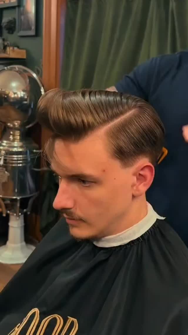 Man with a brown pompadour haircut and side part in a barbershop.