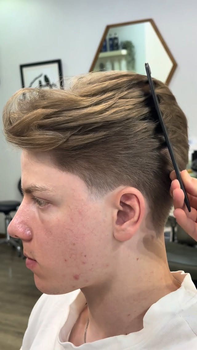Young man with a styled quiff haircut being combed in a salon.