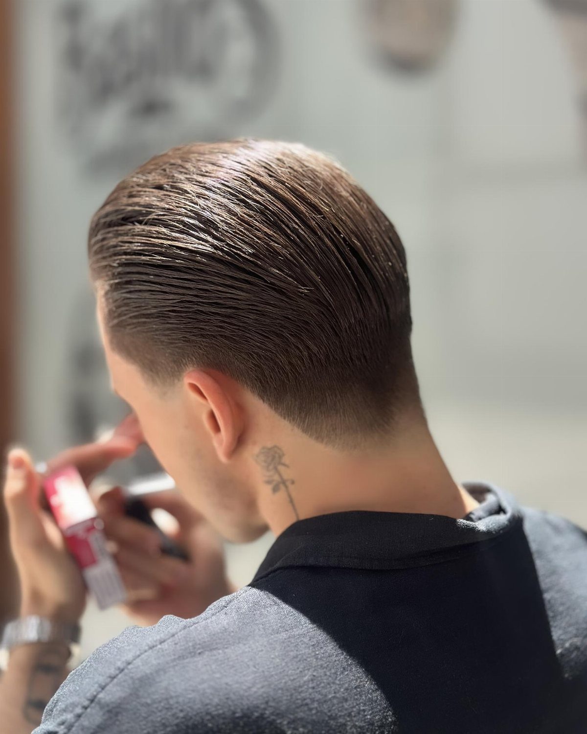 Man with a slick back undercut hairstyle and a small neck tattoo.