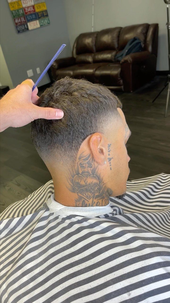 Man with a short fade haircut and neck tattoos in a barbershop setting.