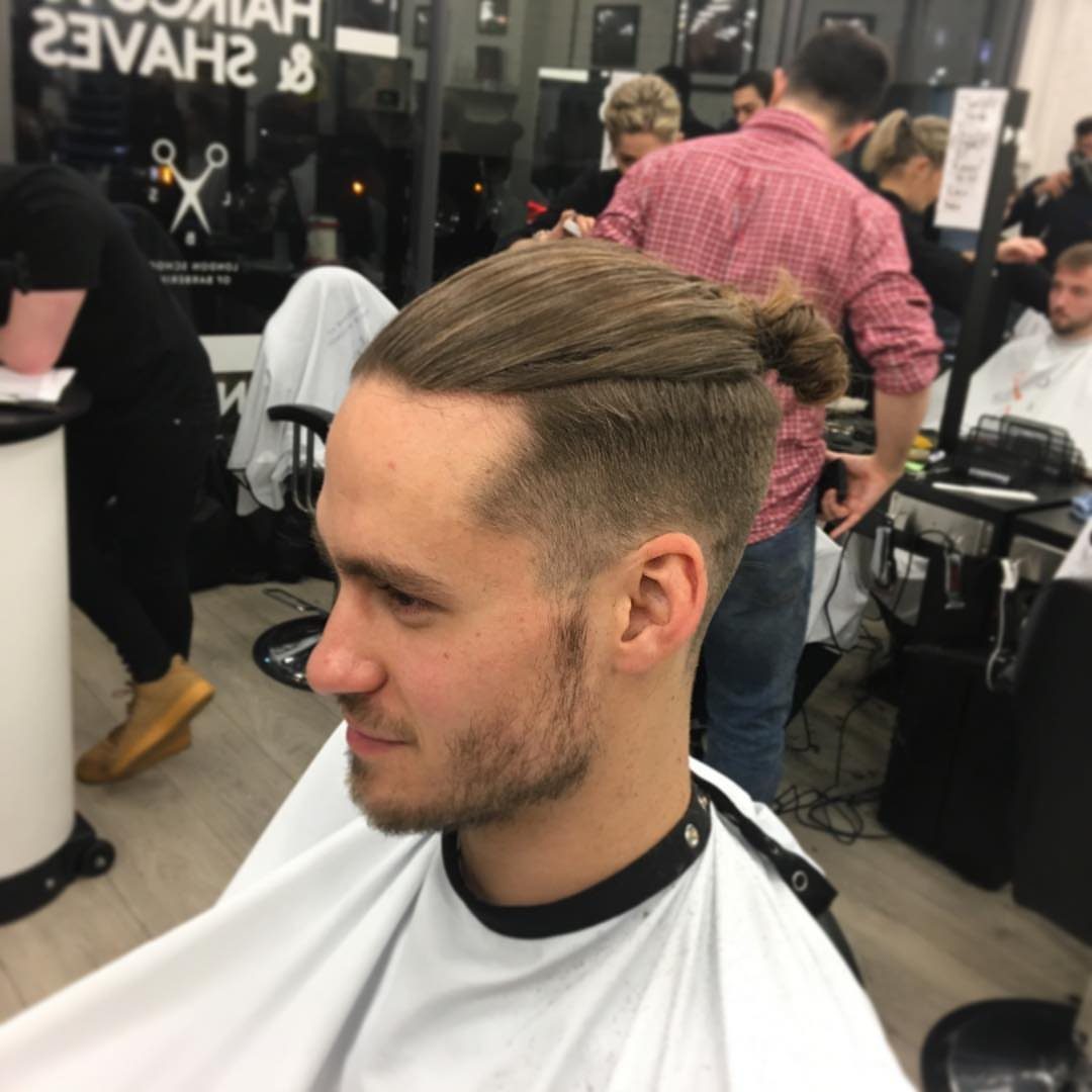 Man with a top knot haircut and shaved sides in a barbershop setting.