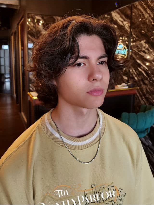 Young man with medium-length wavy brown hair styled in layered cuts.