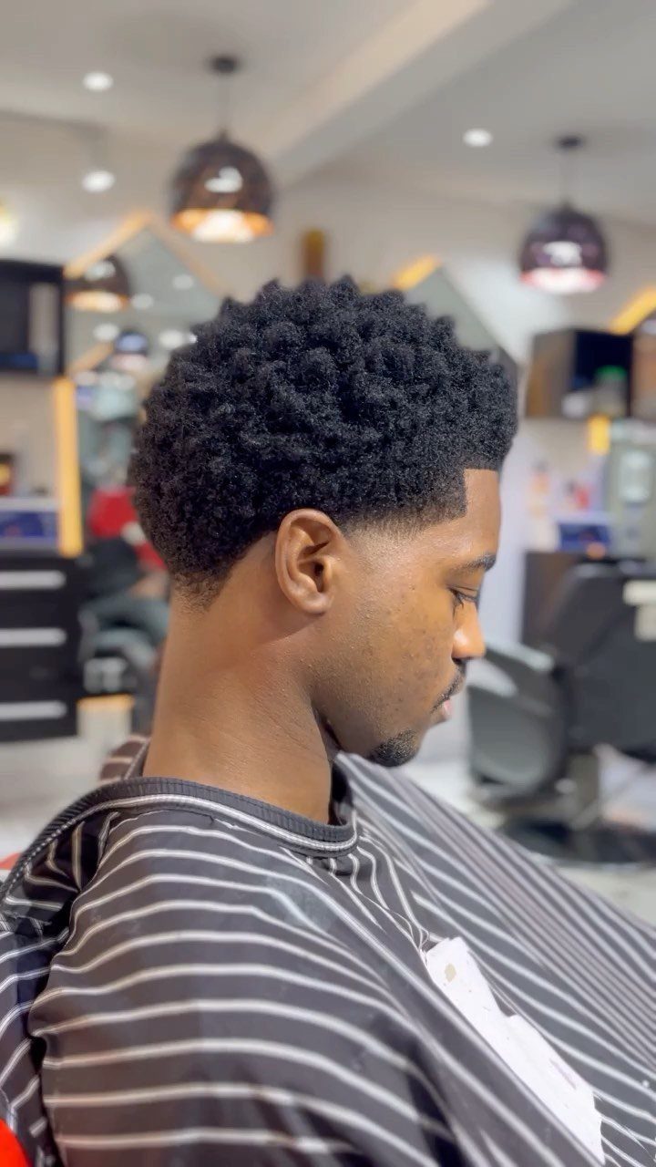 Man with curly black hair and a taper haircut in a barbershop.