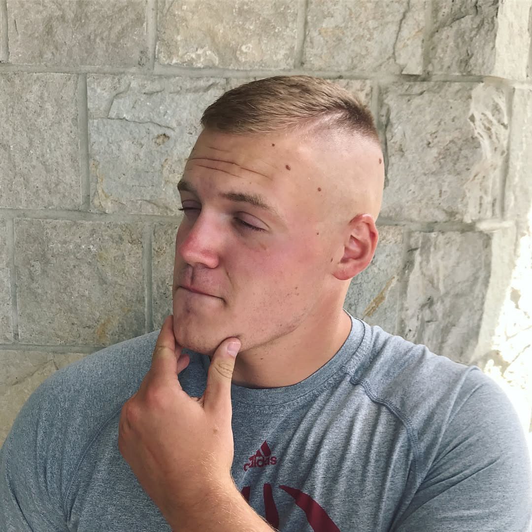 Man with a high and tight haircut posing against a stone wall.