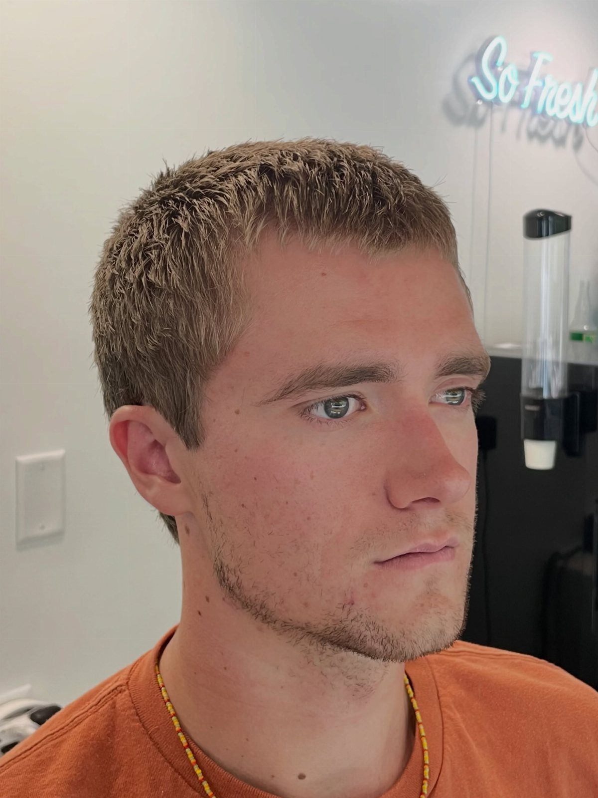 Man with an outgrown buzz cut and short textured brown hair wearing orange shirt
