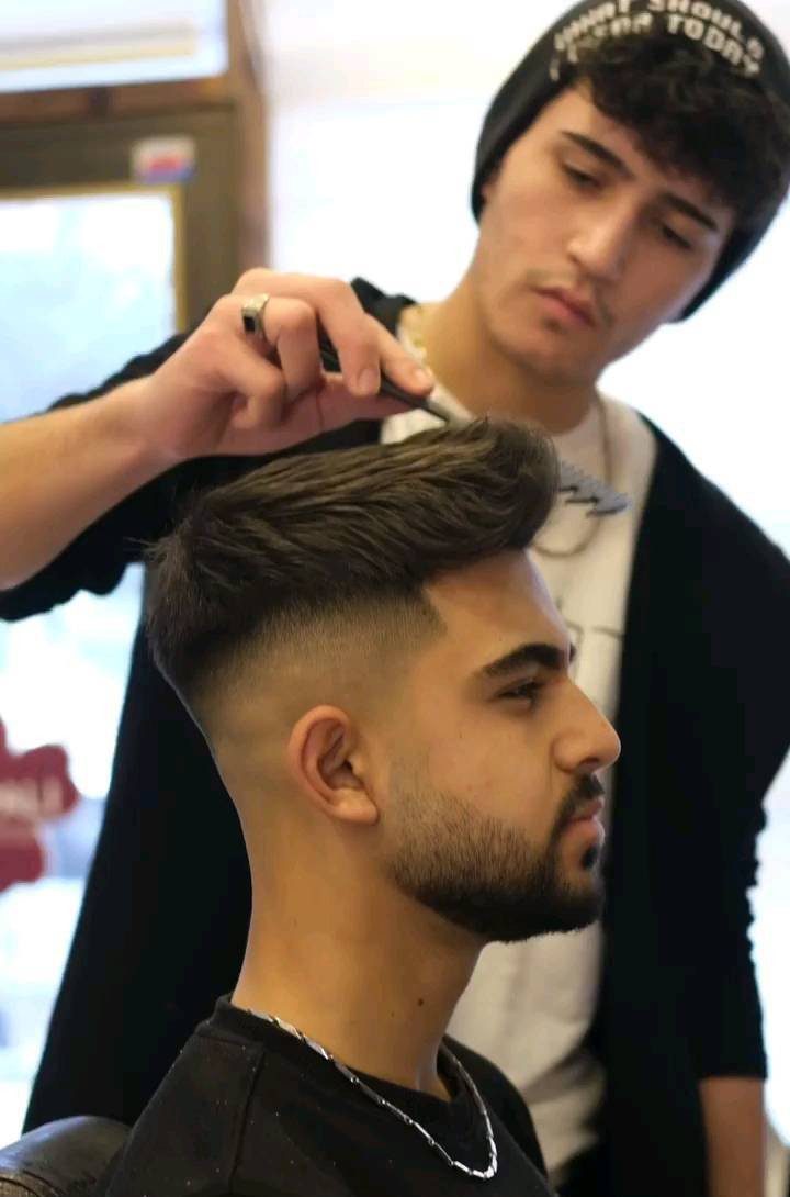 Barber styling a man's quiff haircut with a fade and groomed beard.
