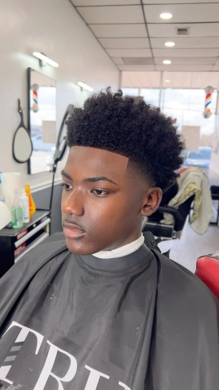 Young Black man with a short high-top fade haircut in a barbershop setting.