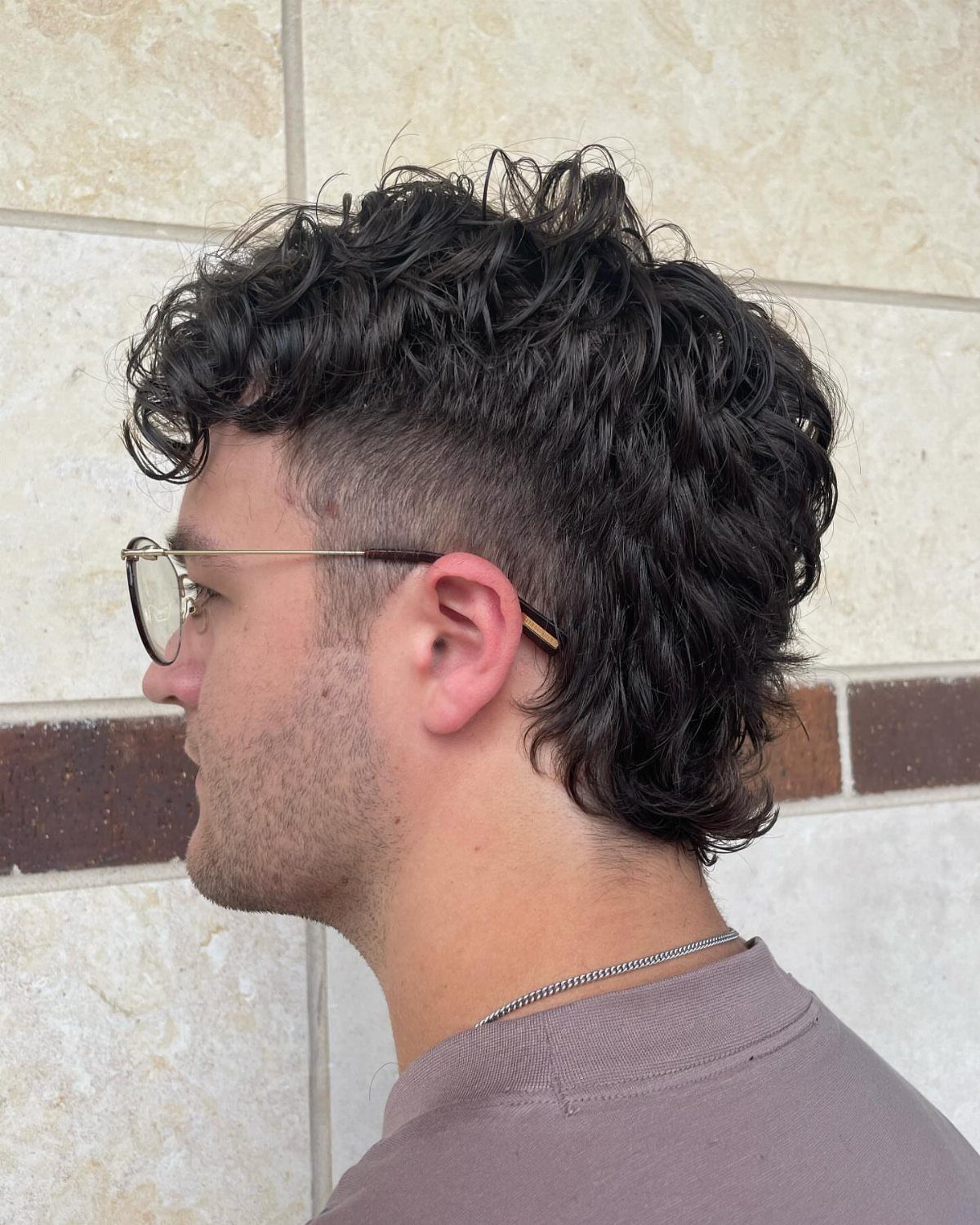 Man with curly dark hair in a short mullet style and glasses.