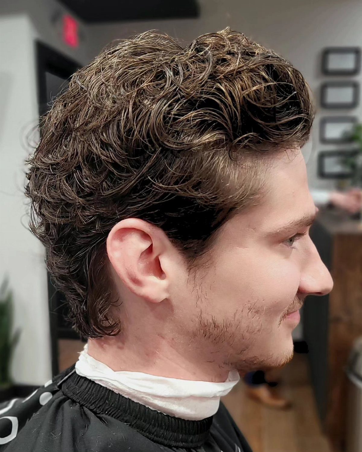 Man with short curly brown hair in a barbershop side profile view