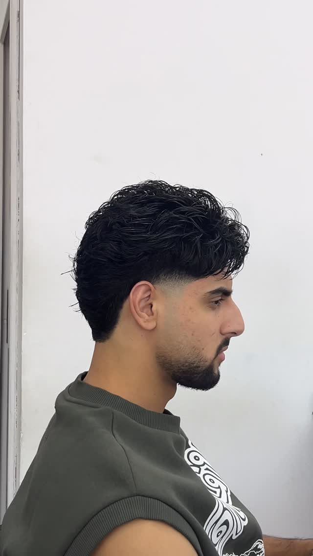 Man with dark wavy hair on top and a clean taper fade haircut.