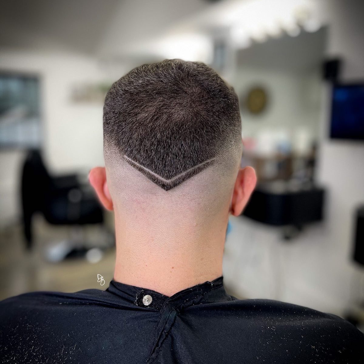 Man's short buzz cut with a V-shaped shaved design on the back neck.