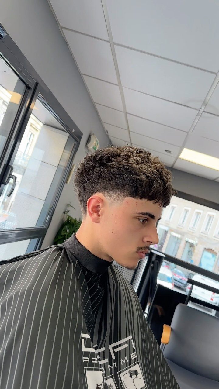 Young man with a French crop haircut and faded sides in a barbershop.