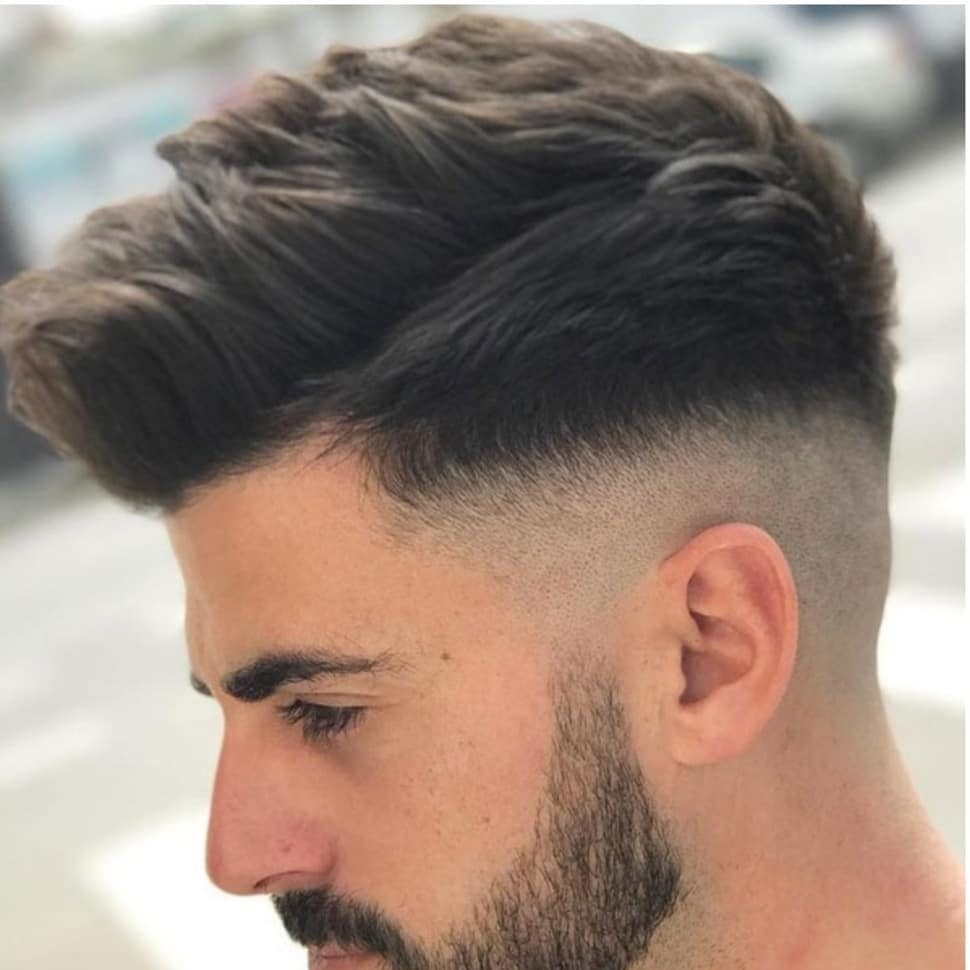 Man with a high skin fade and voluminous swoopy brown hair on top.