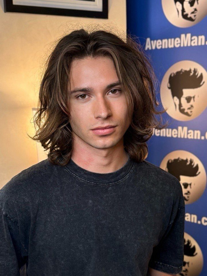 Young man with long straight brown hair parted in the middle wearing grey shirt