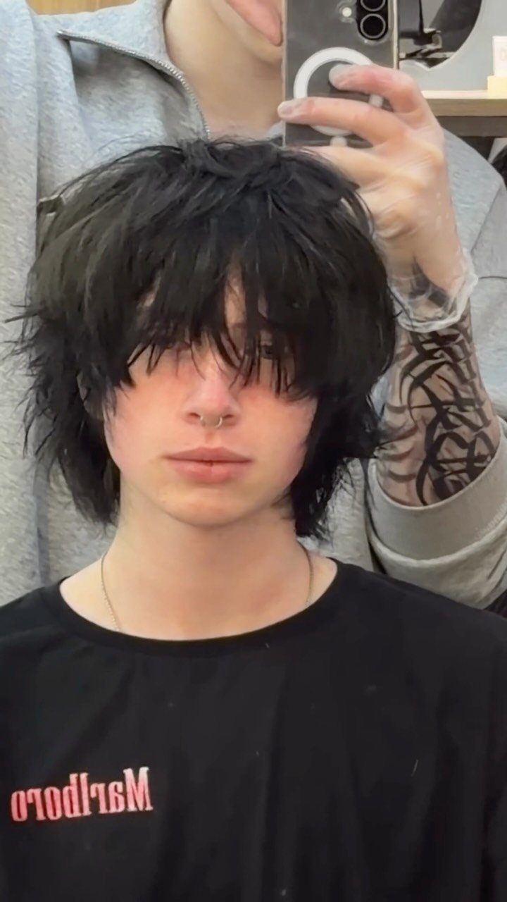 Young man with a shaggy, layered black haircut and long bangs covering eyes