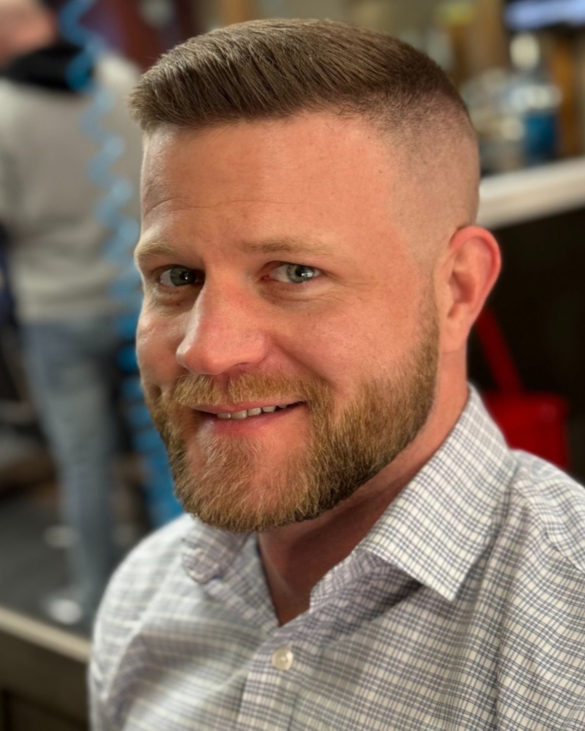 Man with a short straight haircut and groomed beard wearing a checkered shirt.