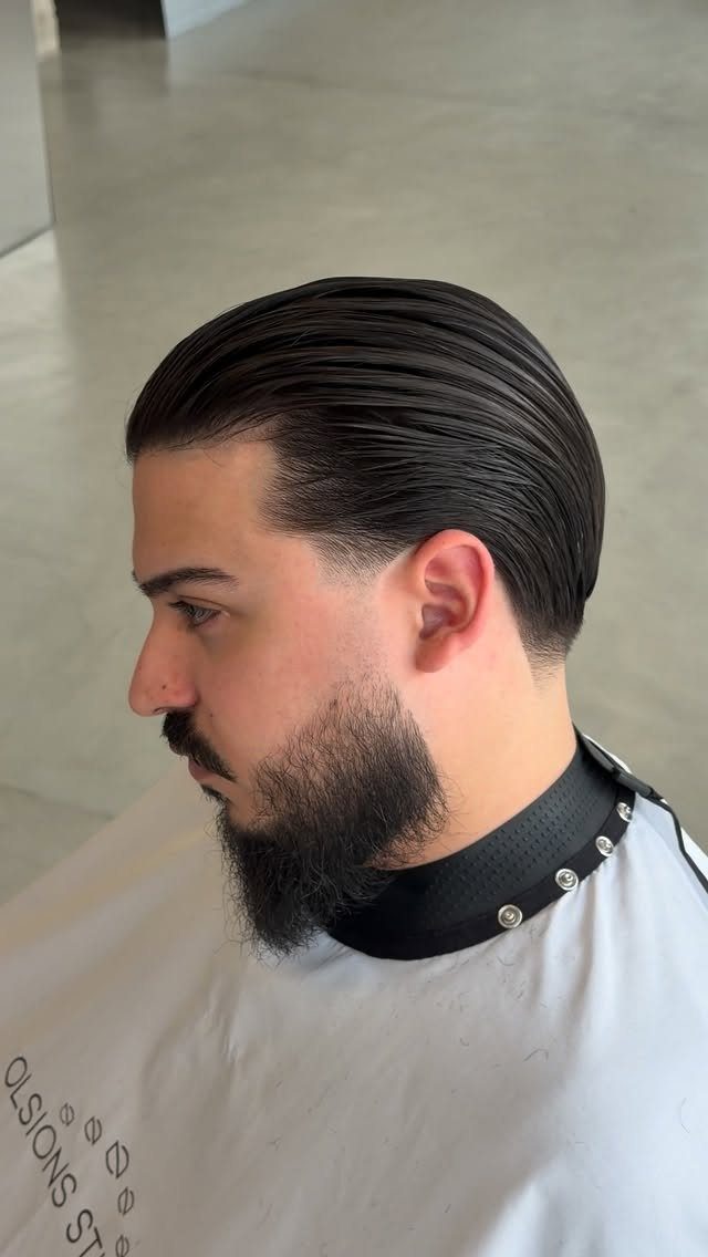 Man with a dark beard and straight black hair styled in a slick back.