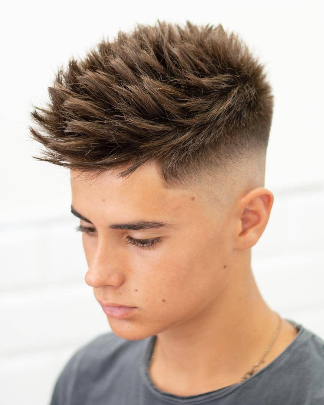 Young man with a tapered spiked haircut and high skin fade on sides.