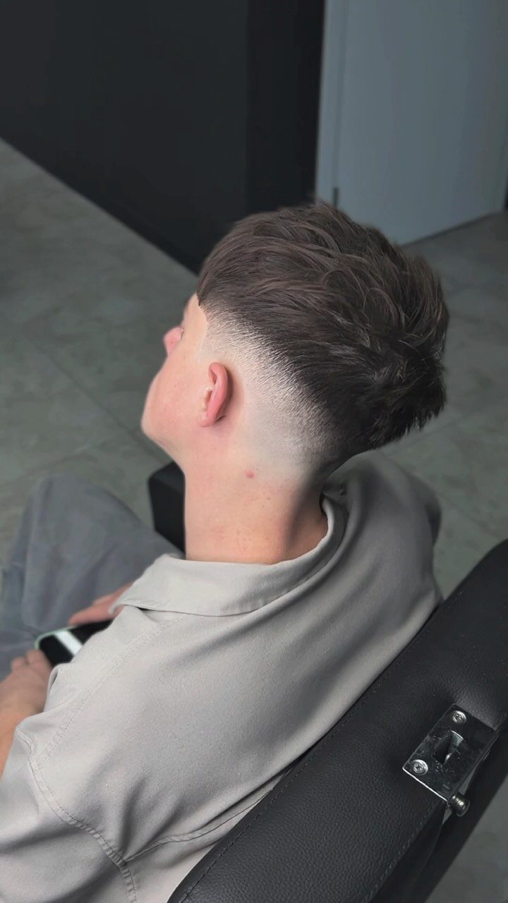 Man with a high skin fade and textured voluminous brown hair styled backwards.