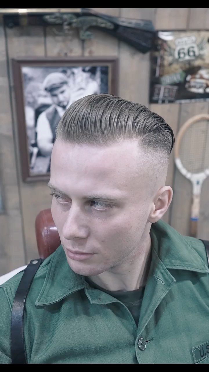 Man with a high undercut haircut and slicked-back straight hair wearing green shirt.