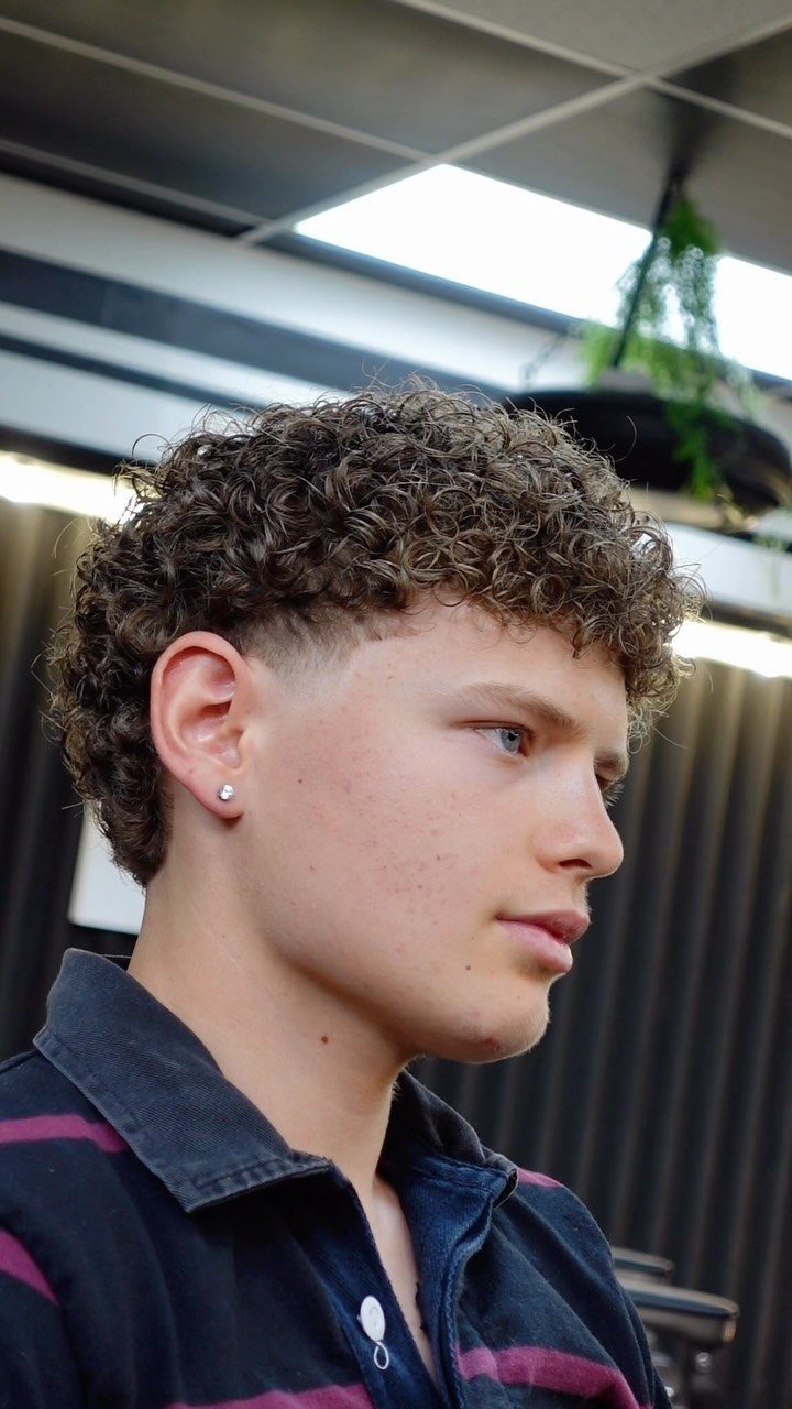 Young man with curly brown hair featuring a taper fade on the sides.