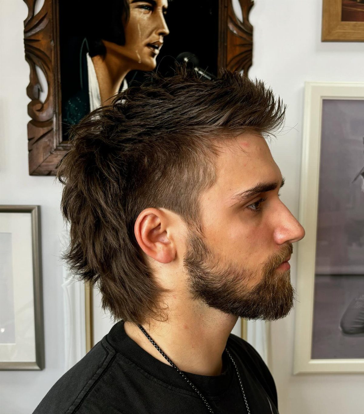 Man with a brown faux hawk hairstyle and beard in a side profile view