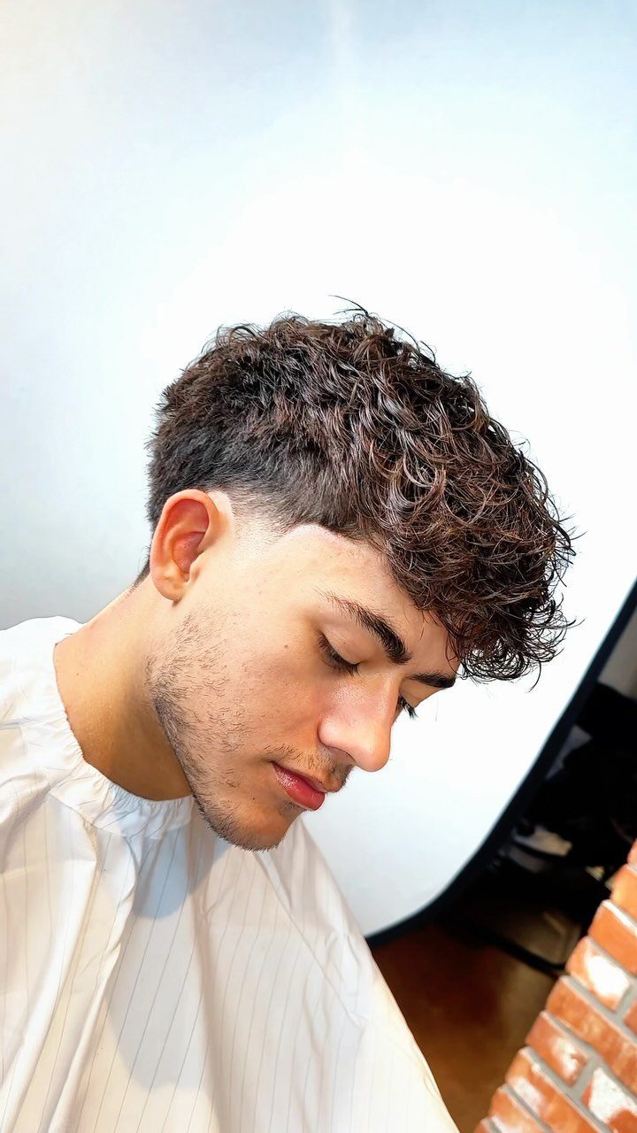 Young man with curly brown hair and a textured fringe over his forehead.