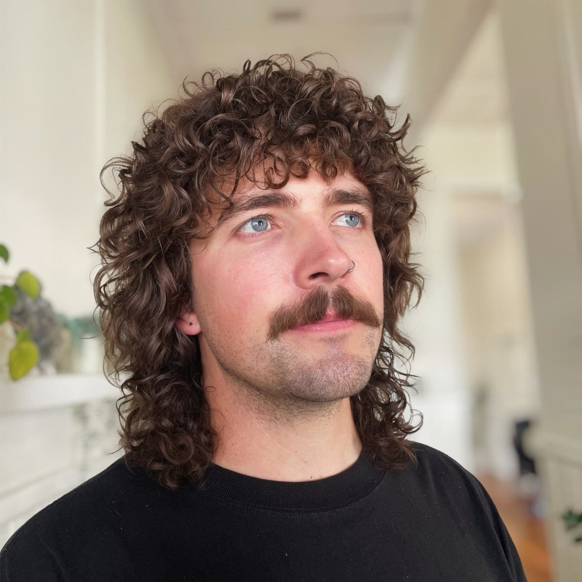Man with medium length natural brown curls and a mustache wearing a black shirt.