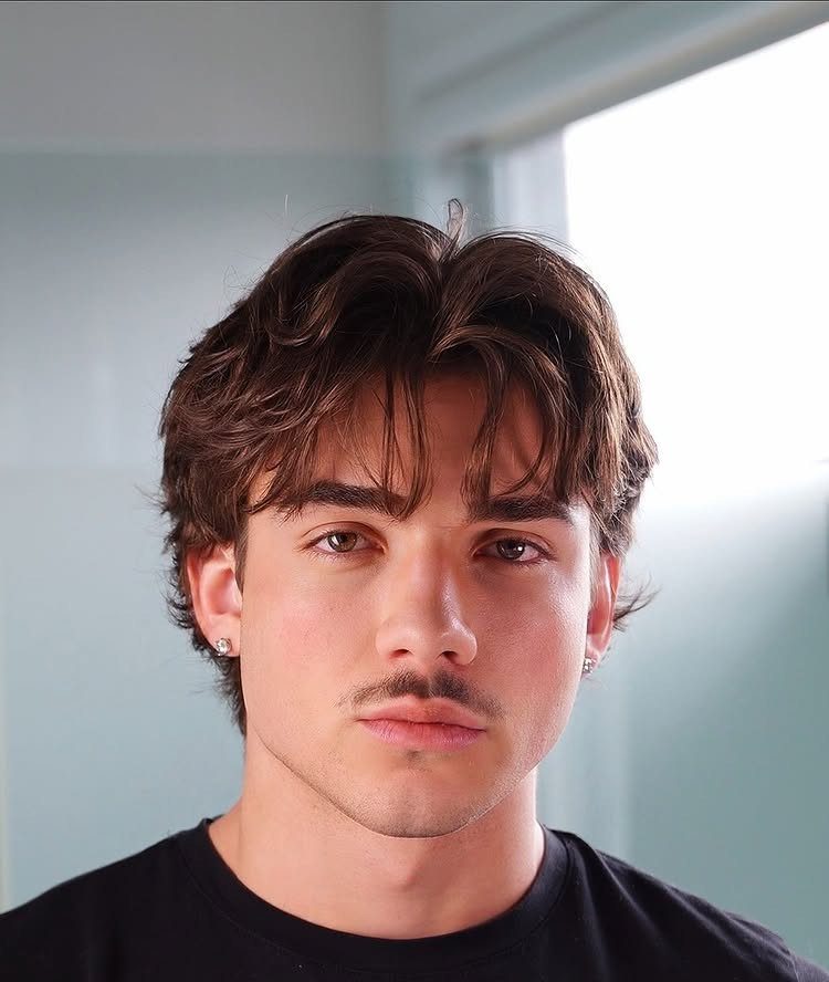 Young man with medium length wavy brown hair and a center part.
