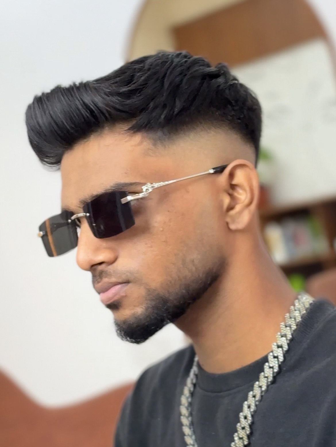 Man with a styled quiff hairstyle, faded sides, sunglasses, and a silver chain.
