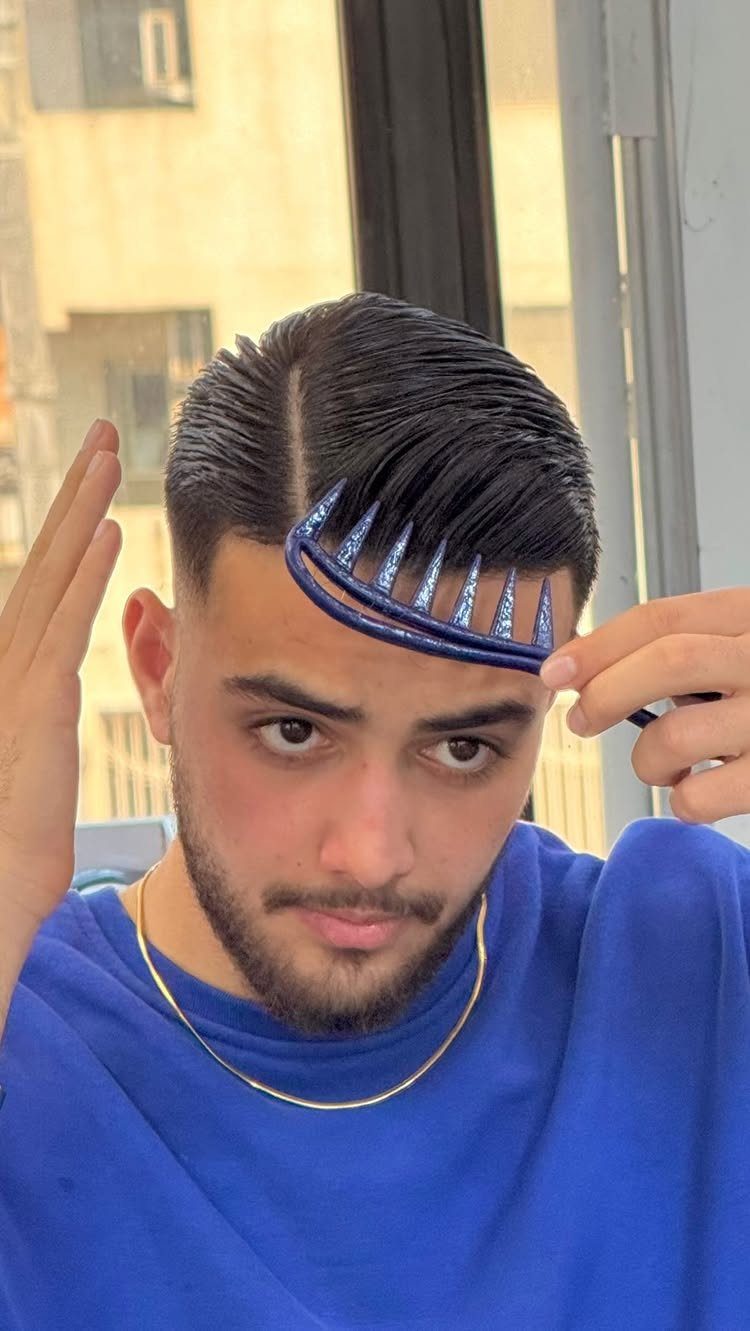 Young man with a side part hairstyle holding a blue comb to his hair.