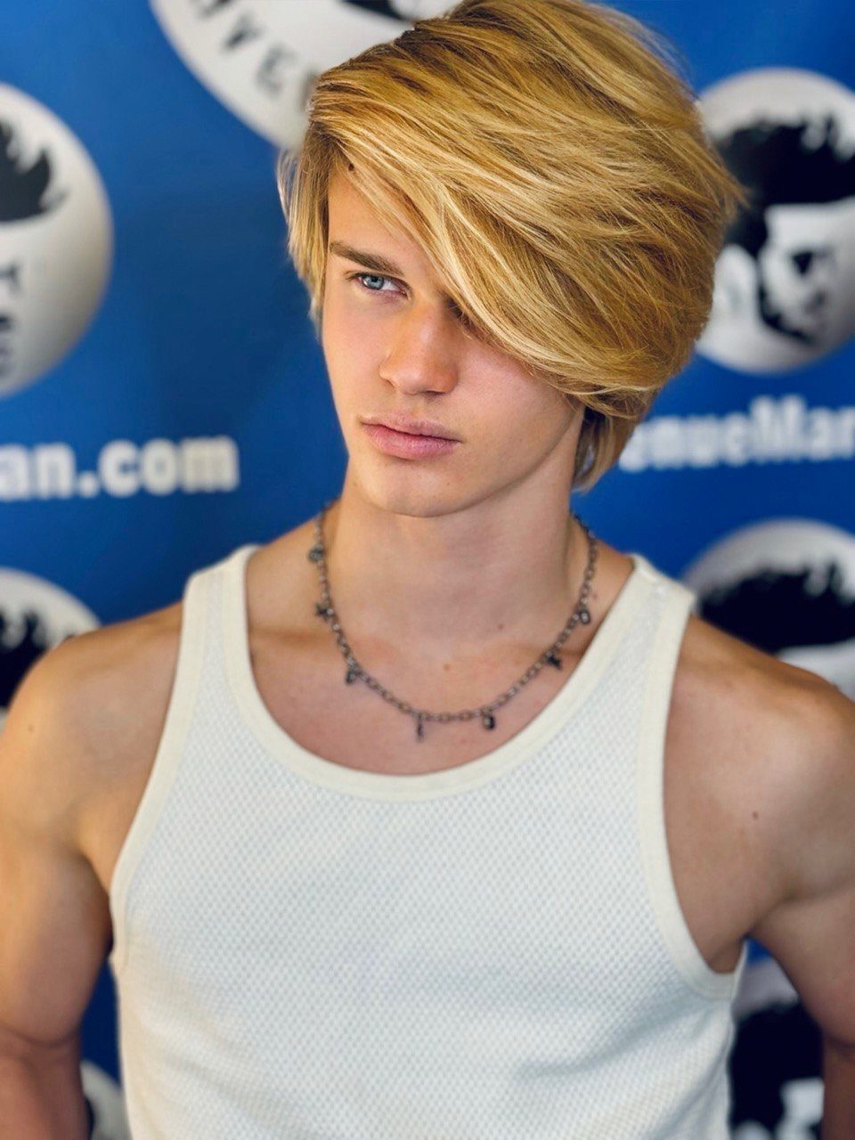 Young man with blonde medium length hair swept across his forehead in a side-swept style.